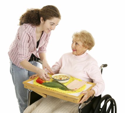 Femme aidant une personne âgée en fauteuil roulant avec un repas.