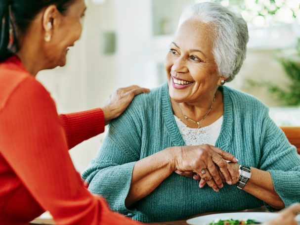Deux femmes souriantes se regardent, partageant un moment convivial autour d'un repas.