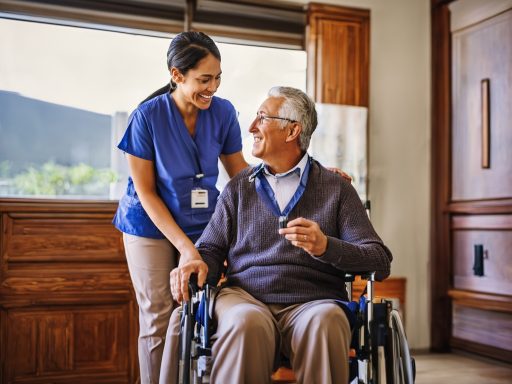 Une aide souriante assiste un homme âgé en fauteuil roulant dans un environnement chaleureux.