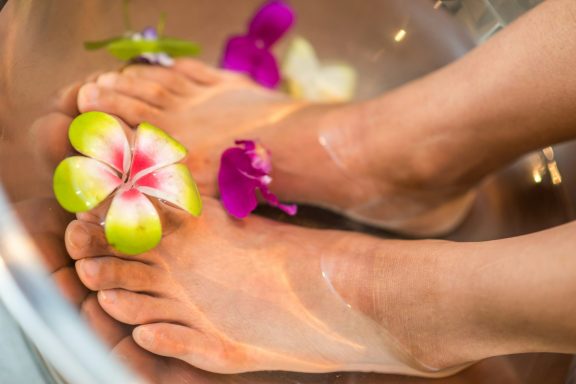 Petits pieds immergés dans l'eau avec des fleurs autour.